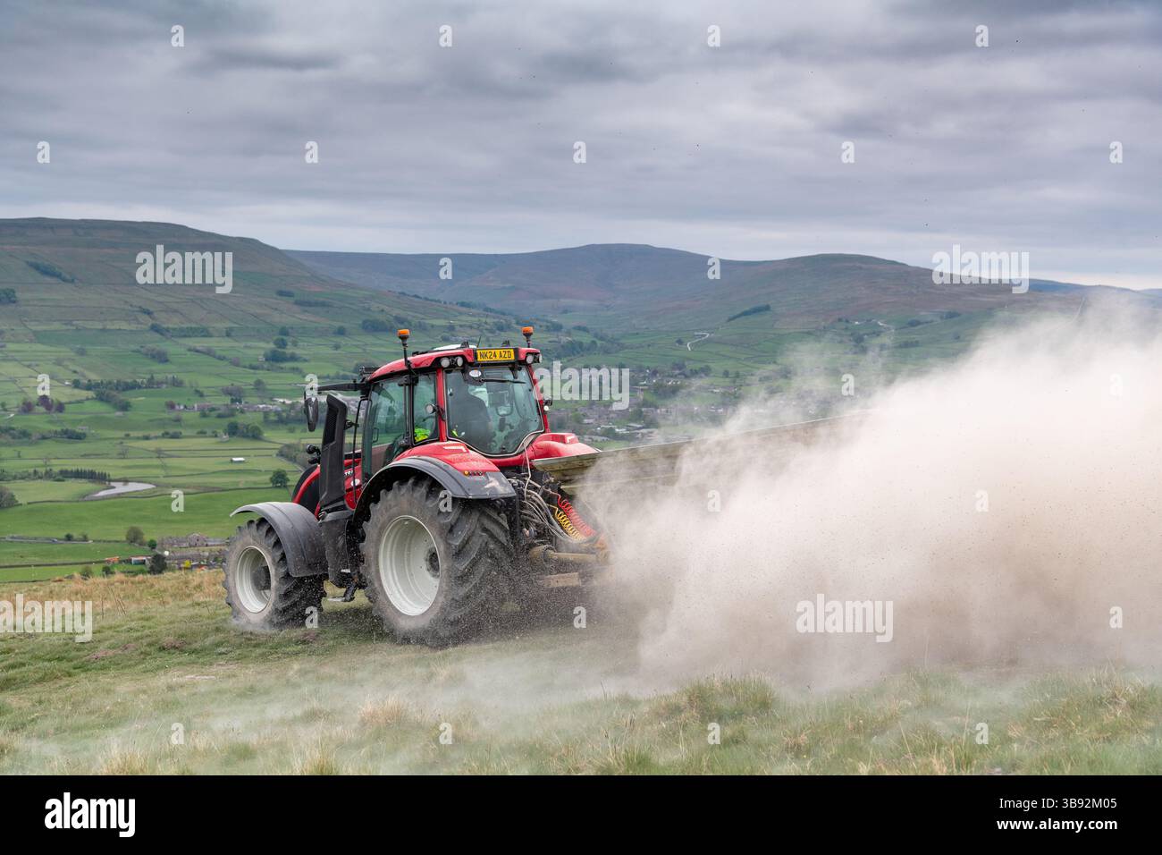 Appaltatore agricolo, alla guida di un trattore Valtra rosso, spalmando calce su un ripido pascolo per migliorare il pH del terreno e la qualità del terreno. Wensley Foto Stock