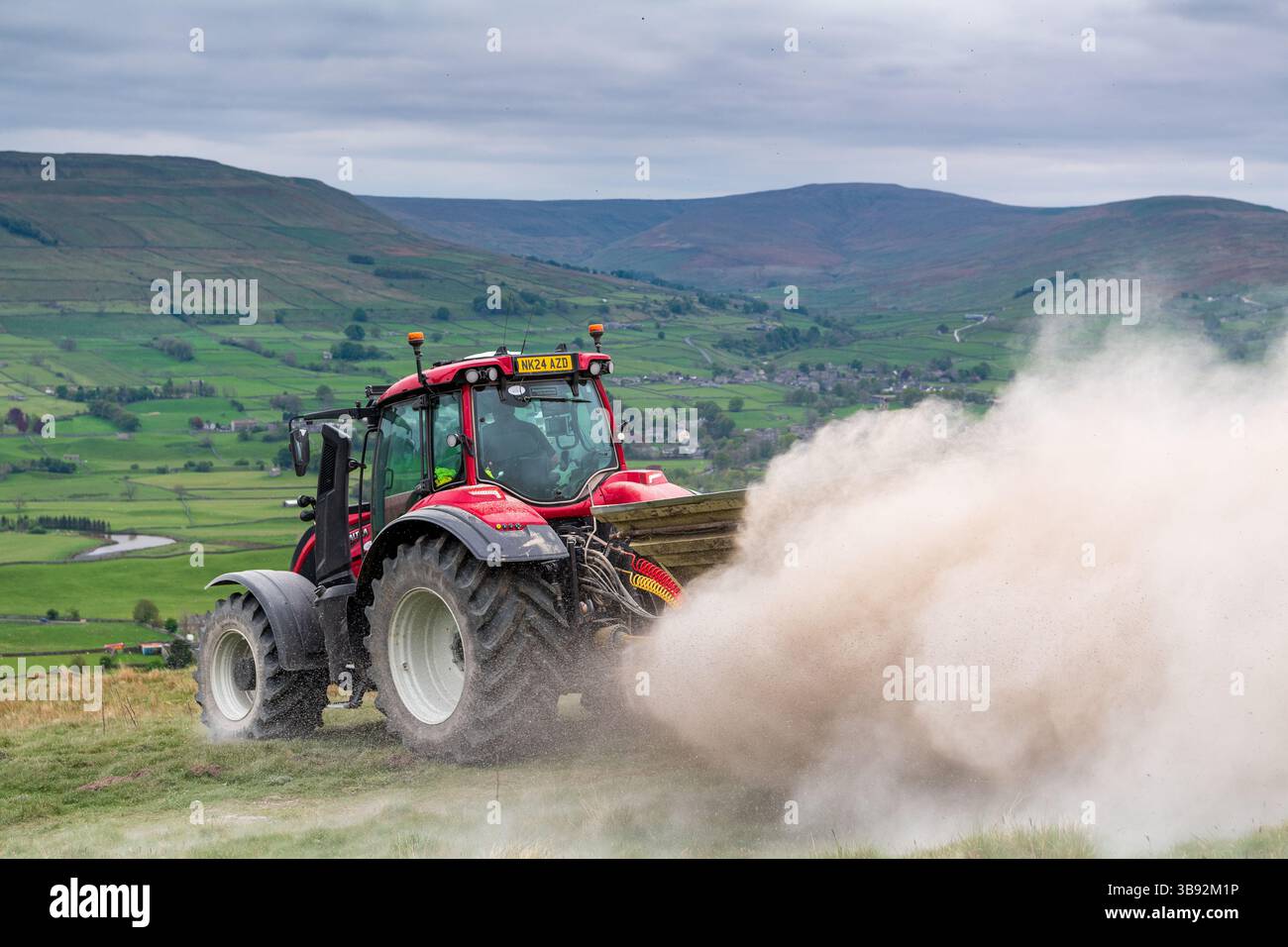 Appaltatore agricolo, alla guida di un trattore Valtra rosso, spalmando calce su un ripido pascolo per migliorare il pH del terreno e la qualità del terreno. Wensley Foto Stock