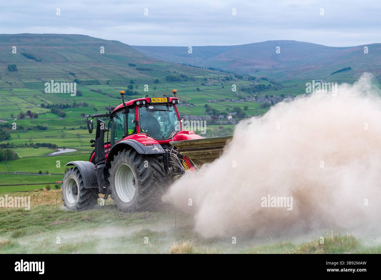 Appaltatore agricolo, alla guida di un trattore Valtra rosso, spalmando calce su un ripido pascolo per migliorare il pH del terreno e la qualità del terreno. Wensley Foto Stock