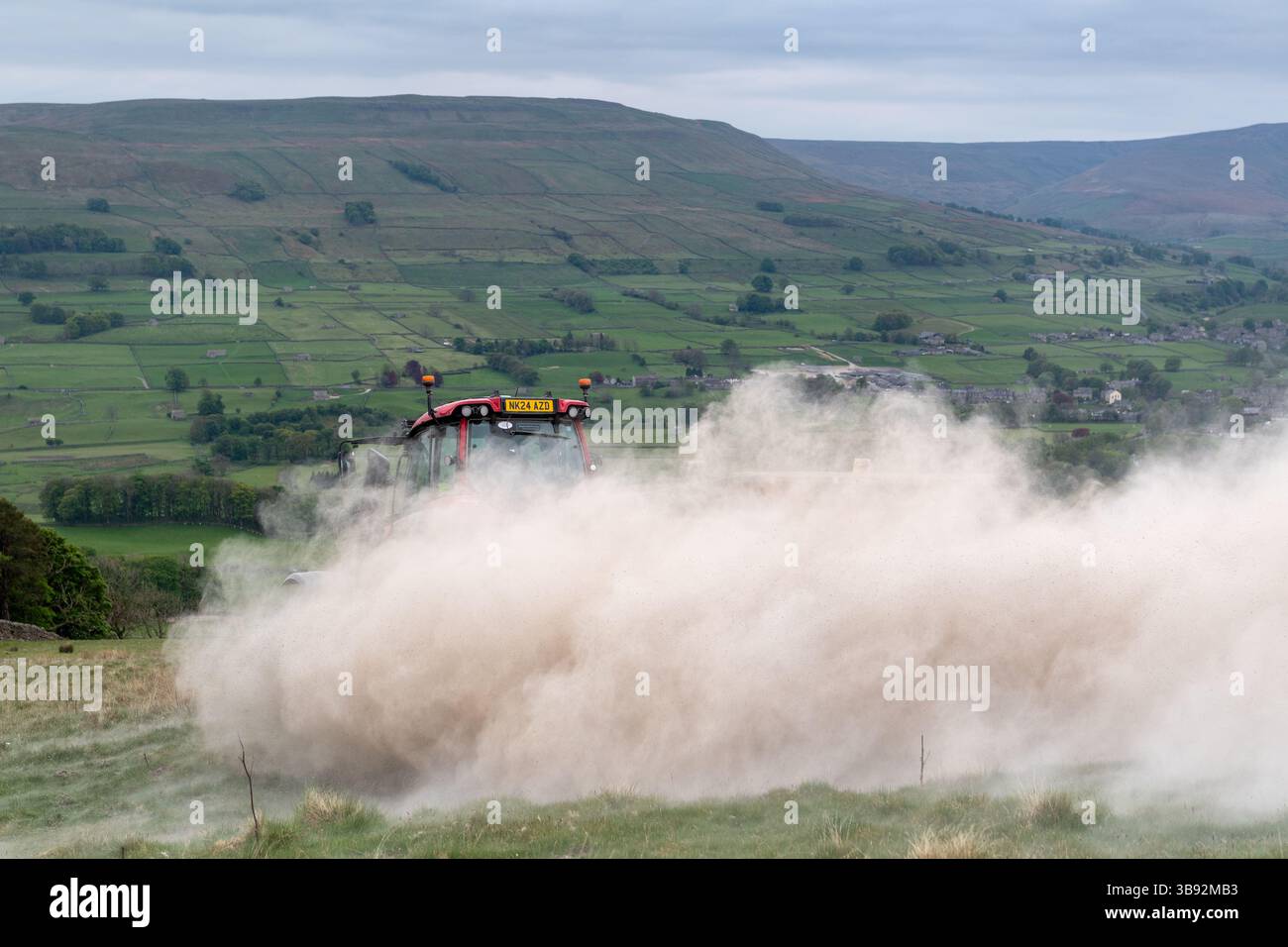 Appaltatore agricolo, alla guida di un trattore Valtra rosso, spalmando calce su un ripido pascolo per migliorare il pH del terreno e la qualità del terreno. Wensley Foto Stock