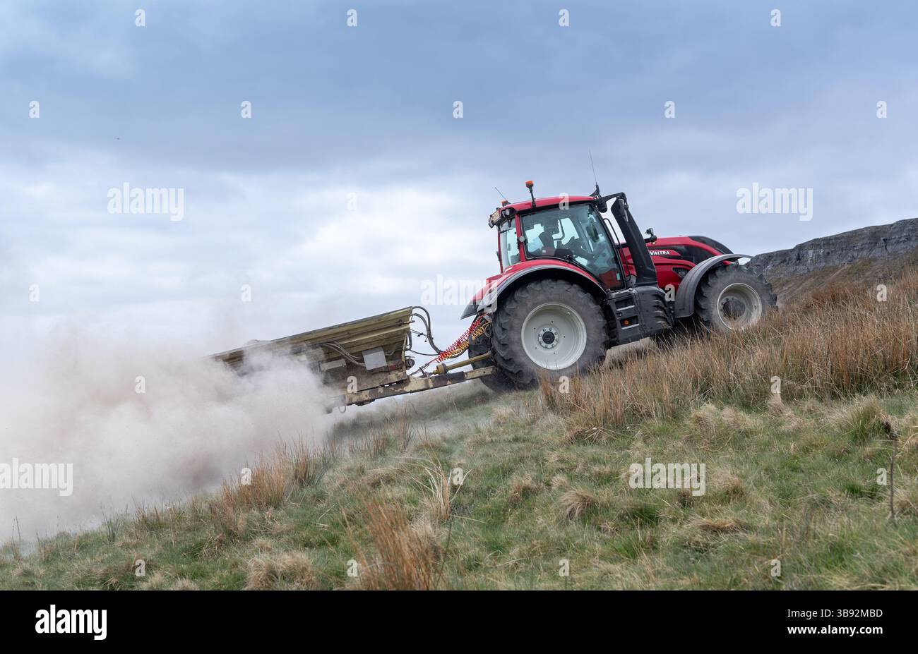 Appaltatore agricolo, alla guida di un trattore Valtra rosso, spalmando calce su un ripido pascolo per migliorare il pH del terreno e la qualità del terreno. Wensley Foto Stock