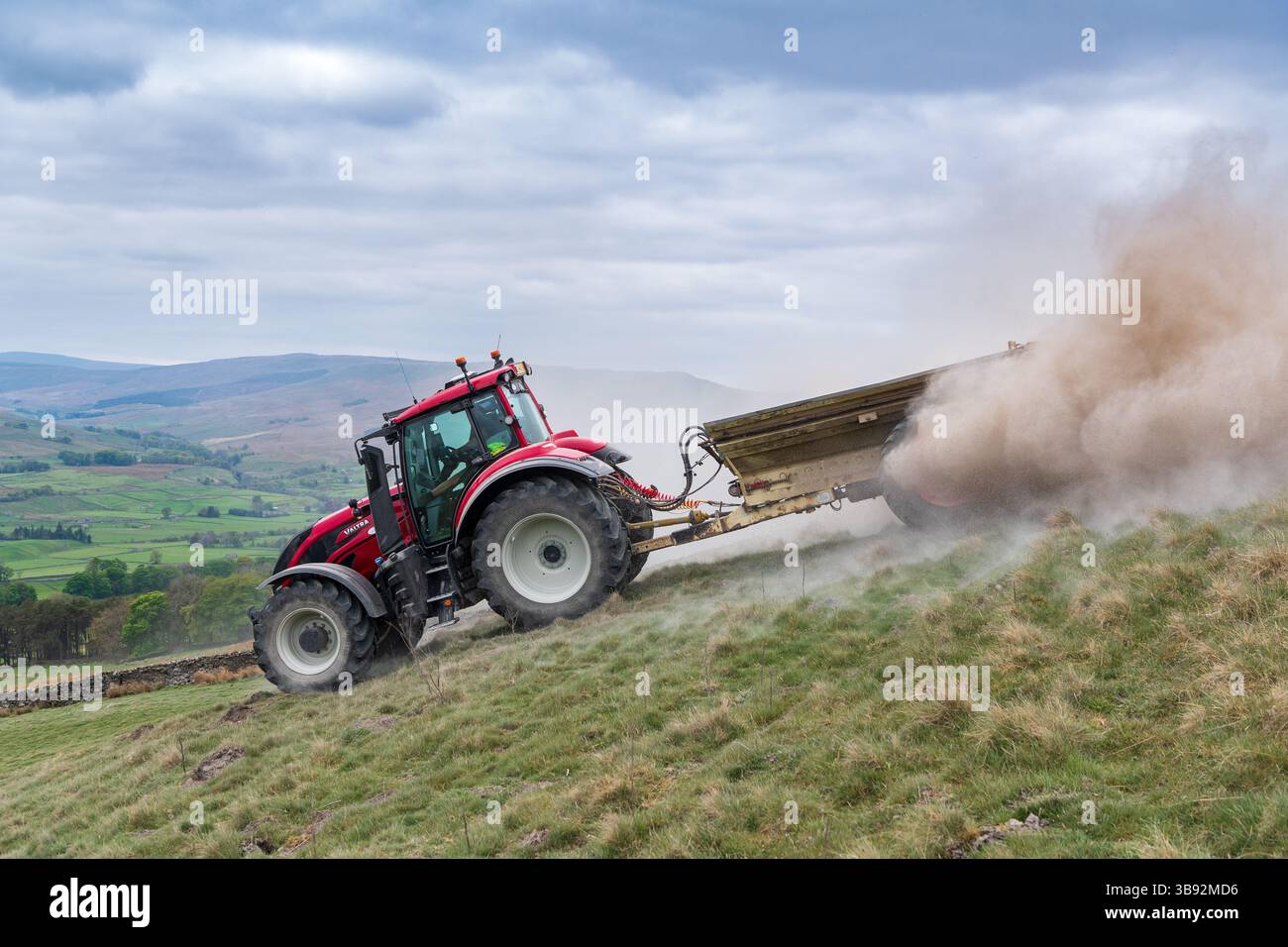 Appaltatore agricolo, alla guida di un trattore Valtra rosso, spalmando calce su un ripido pascolo per migliorare il pH del terreno e la qualità del terreno. Wensley Foto Stock