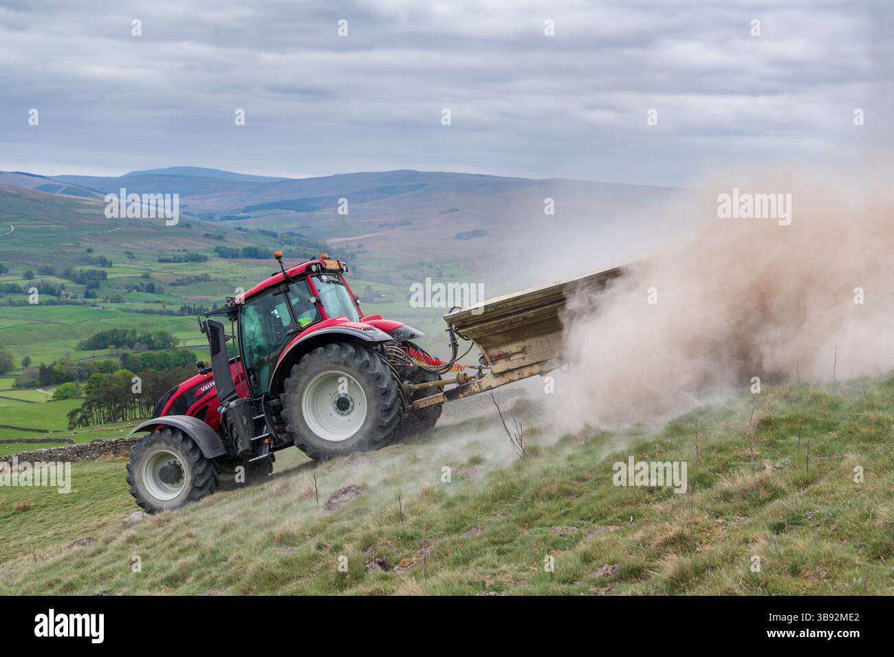 Appaltatore agricolo, alla guida di un trattore Valtra rosso, spalmando calce su un ripido pascolo per migliorare il pH del terreno e la qualità del terreno. Wensley Foto Stock