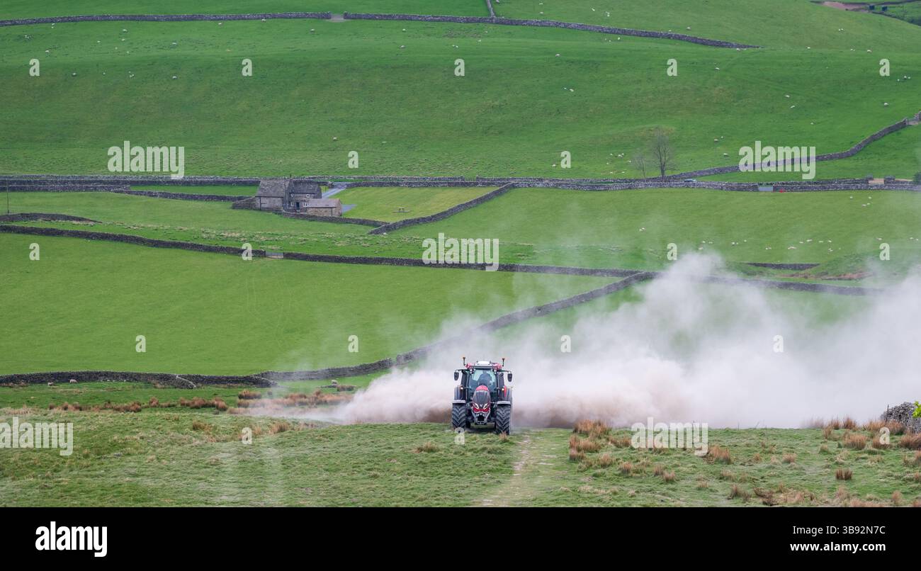 Appaltatore agricolo, alla guida di un trattore Valtra rosso, spalmando calce su un ripido pascolo per migliorare il pH del terreno e la qualità del terreno. Wensley Foto Stock