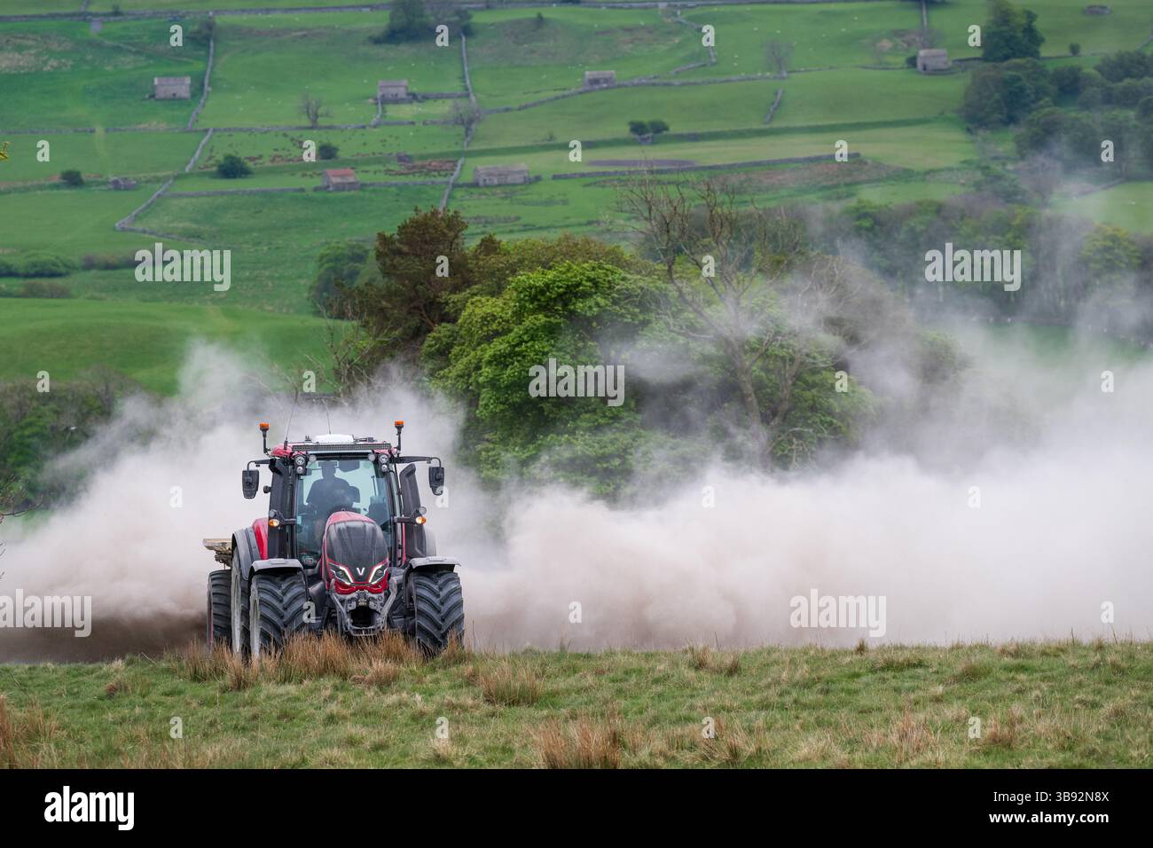Appaltatore agricolo, alla guida di un trattore Valtra rosso, spalmando calce su un ripido pascolo per migliorare il pH del terreno e la qualità del terreno. Wensley Foto Stock