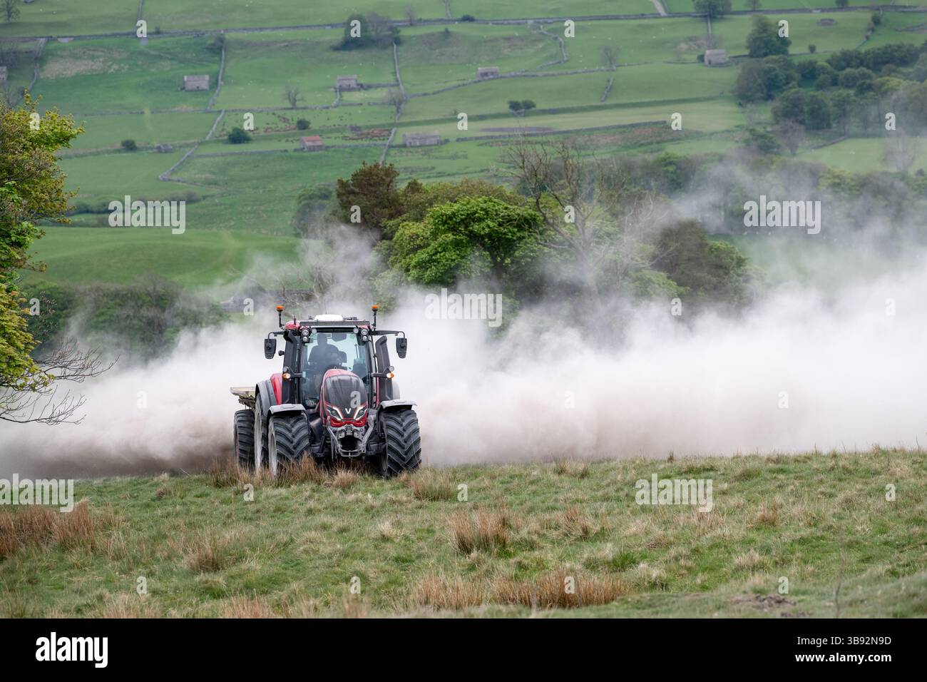 Appaltatore agricolo, alla guida di un trattore Valtra rosso, spalmando calce su un ripido pascolo per migliorare il pH del terreno e la qualità del terreno. Wensley Foto Stock
