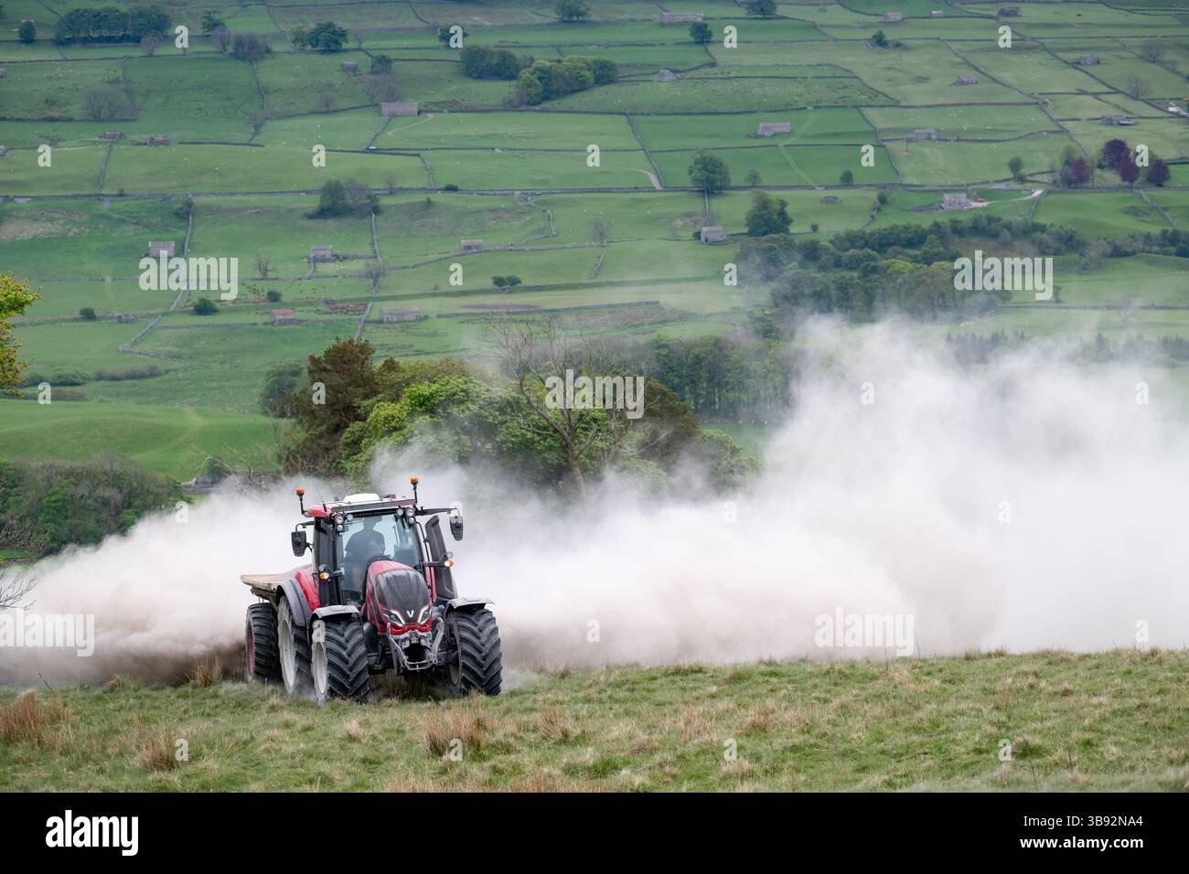 Appaltatore agricolo, alla guida di un trattore Valtra rosso, spalmando calce su un ripido pascolo per migliorare il pH del terreno e la qualità del terreno. Wensley Foto Stock