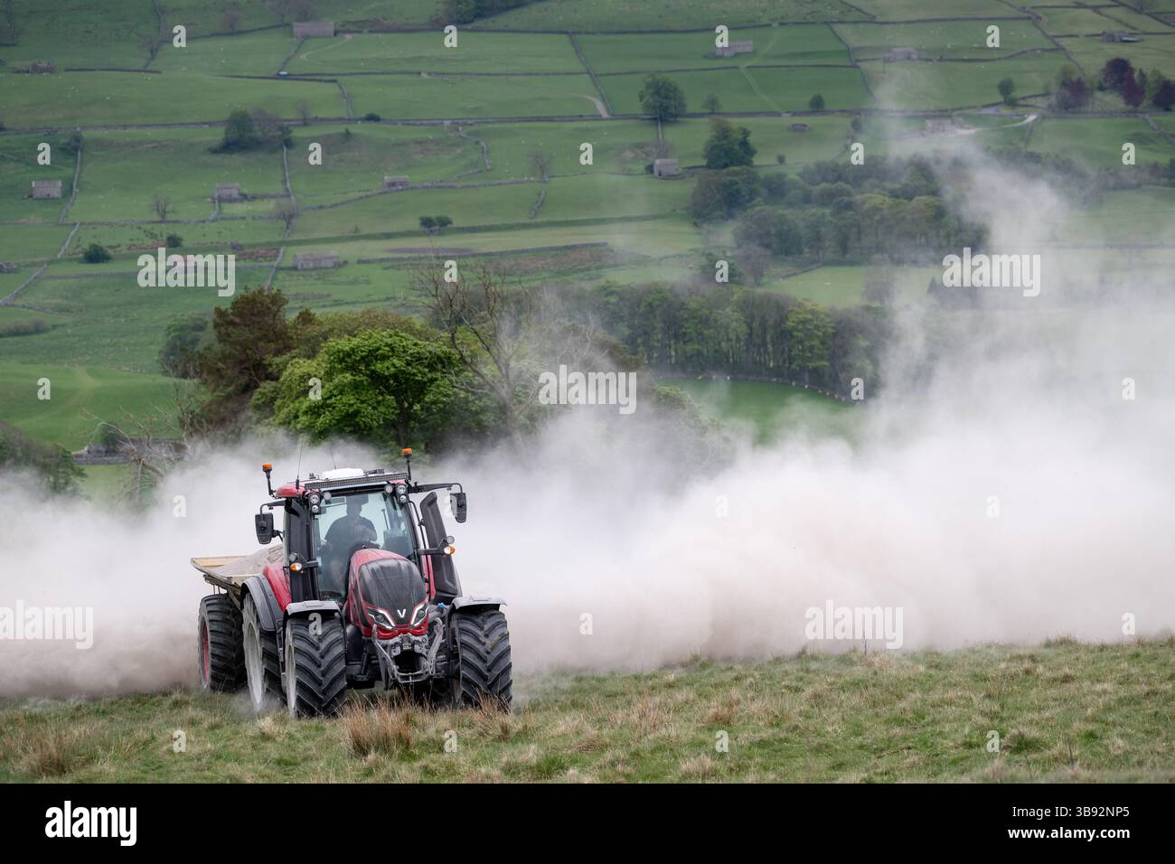 Appaltatore agricolo, alla guida di un trattore Valtra rosso, spalmando calce su un ripido pascolo per migliorare il pH del terreno e la qualità del terreno. Wensley Foto Stock