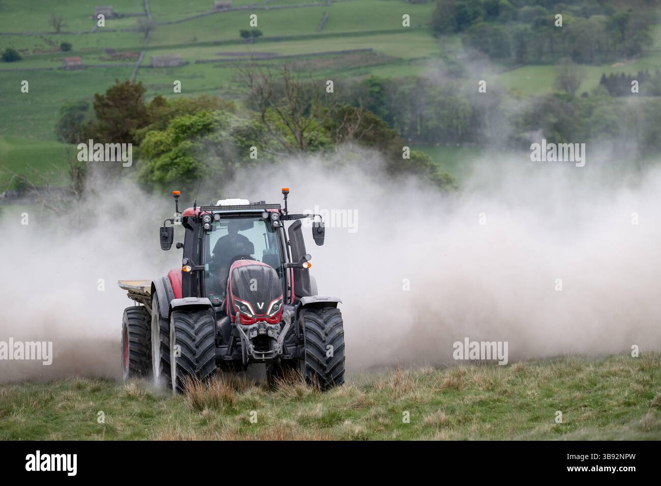 Appaltatore agricolo, alla guida di un trattore Valtra rosso, spalmando calce su un ripido pascolo per migliorare il pH del terreno e la qualità del terreno. Wensley Foto Stock