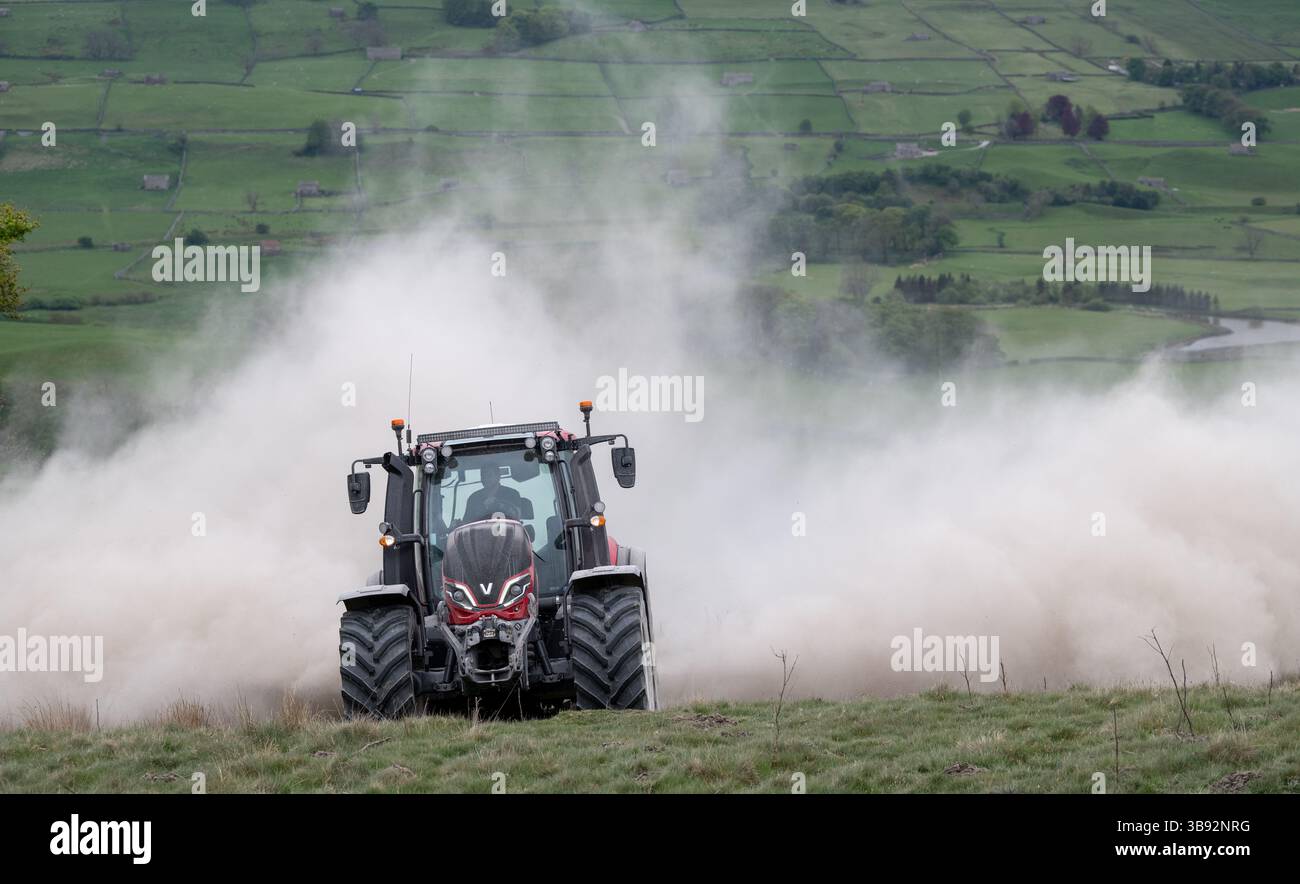Appaltatore agricolo, alla guida di un trattore Valtra rosso, spalmando calce su un ripido pascolo per migliorare il pH del terreno e la qualità del terreno. Wensley Foto Stock