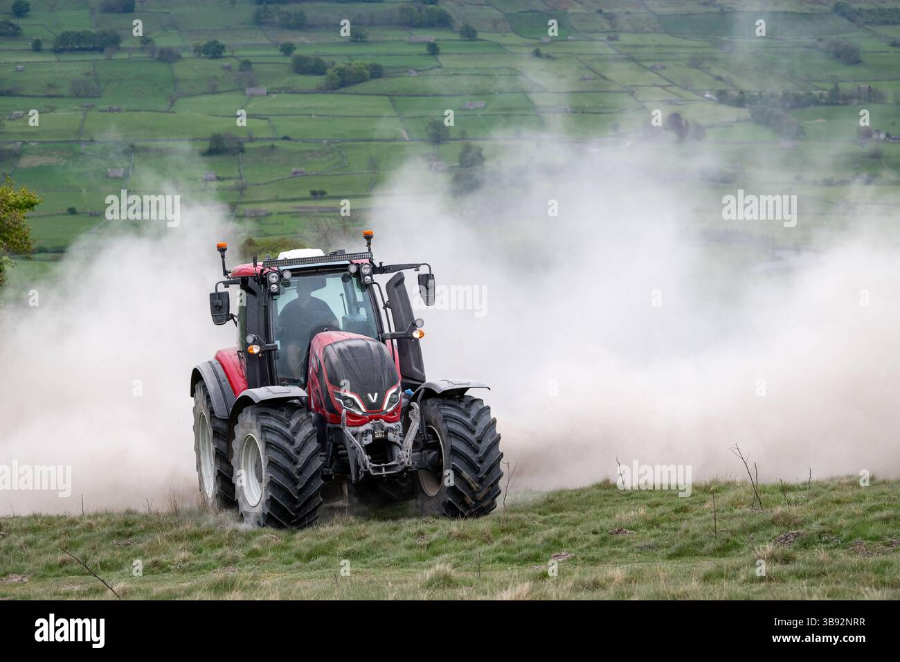 Appaltatore agricolo, alla guida di un trattore Valtra rosso, spalmando calce su un ripido pascolo per migliorare il pH del terreno e la qualità del terreno. Wensley Foto Stock