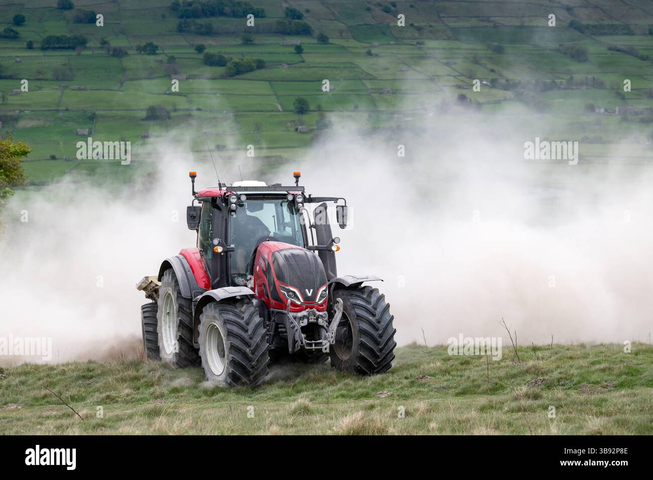Appaltatore agricolo, alla guida di un trattore Valtra rosso, spalmando calce su un ripido pascolo per migliorare il pH del terreno e la qualità del terreno. Wensley Foto Stock