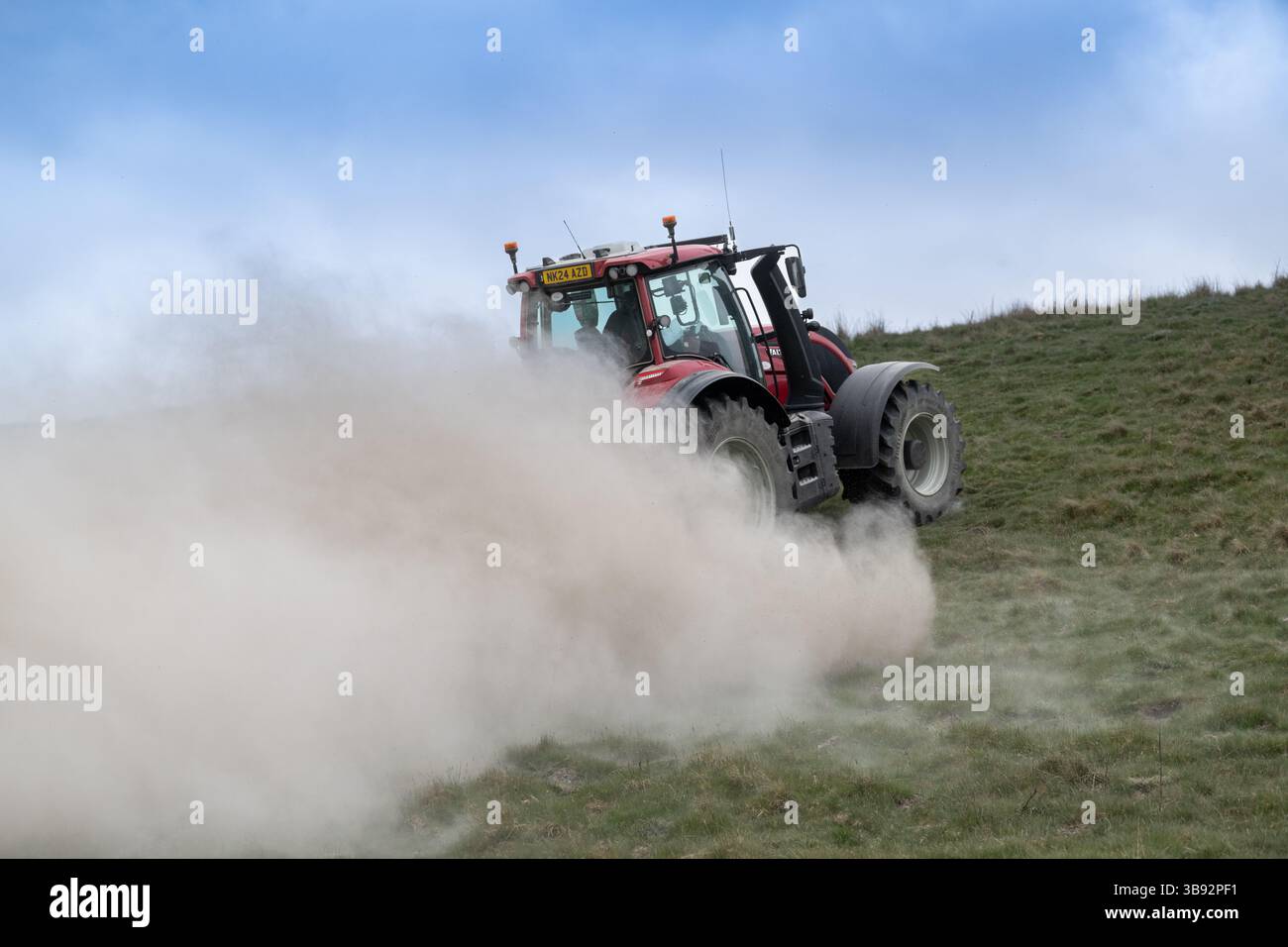 Appaltatore agricolo, alla guida di un trattore Valtra rosso, spalmando calce su un ripido pascolo per migliorare il pH del terreno e la qualità del terreno. Wensley Foto Stock
