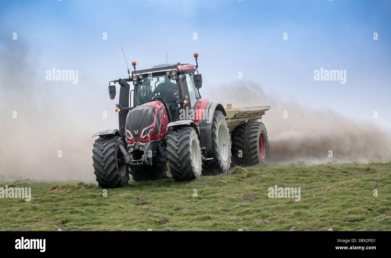 Appaltatore agricolo, alla guida di un trattore Valtra rosso, spalmando calce su un ripido pascolo per migliorare il pH del terreno e la qualità del terreno. Wensley Foto Stock