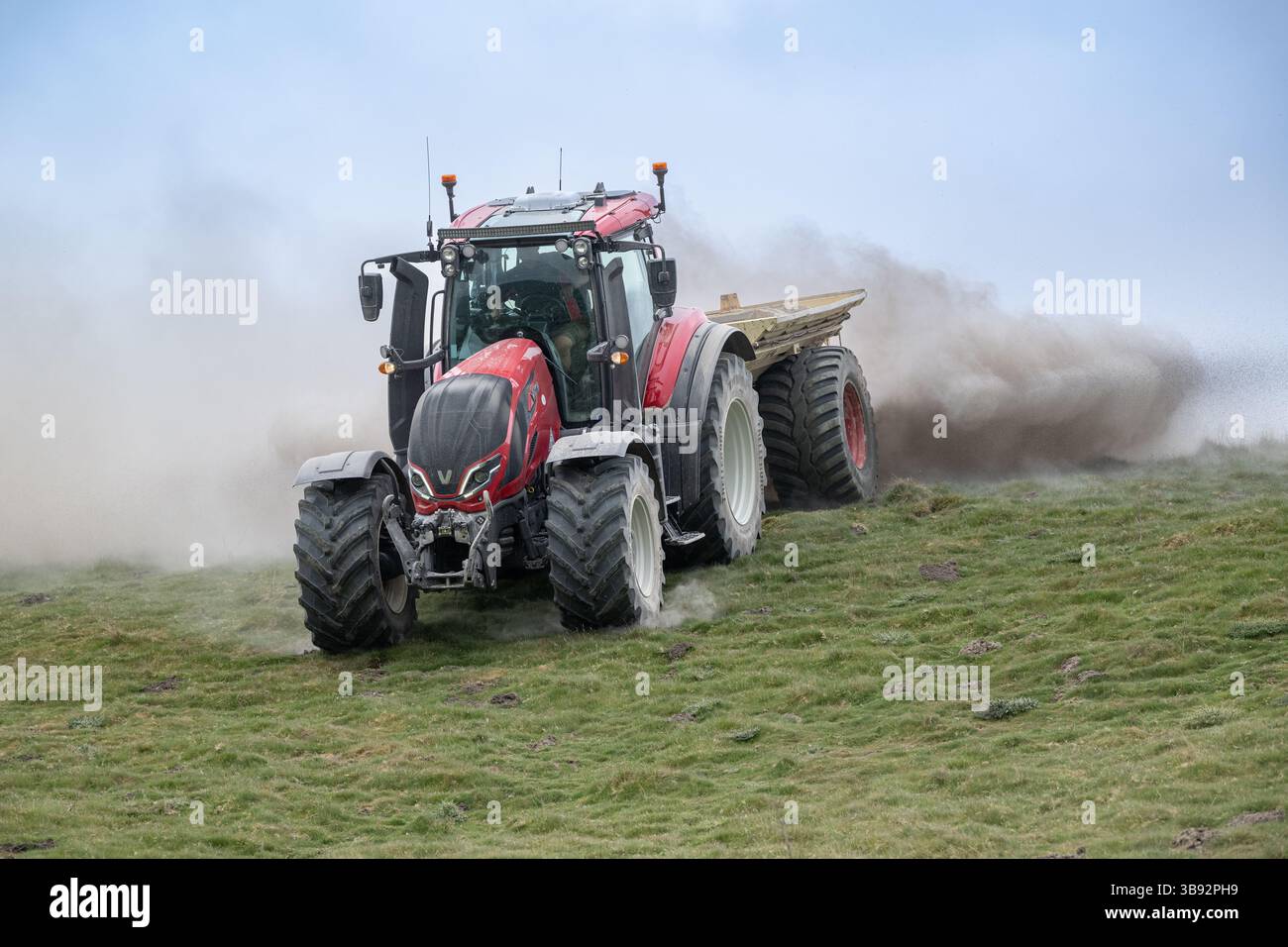 Appaltatore agricolo, alla guida di un trattore Valtra rosso, spalmando calce su un ripido pascolo per migliorare il pH del terreno e la qualità del terreno. Wensley Foto Stock