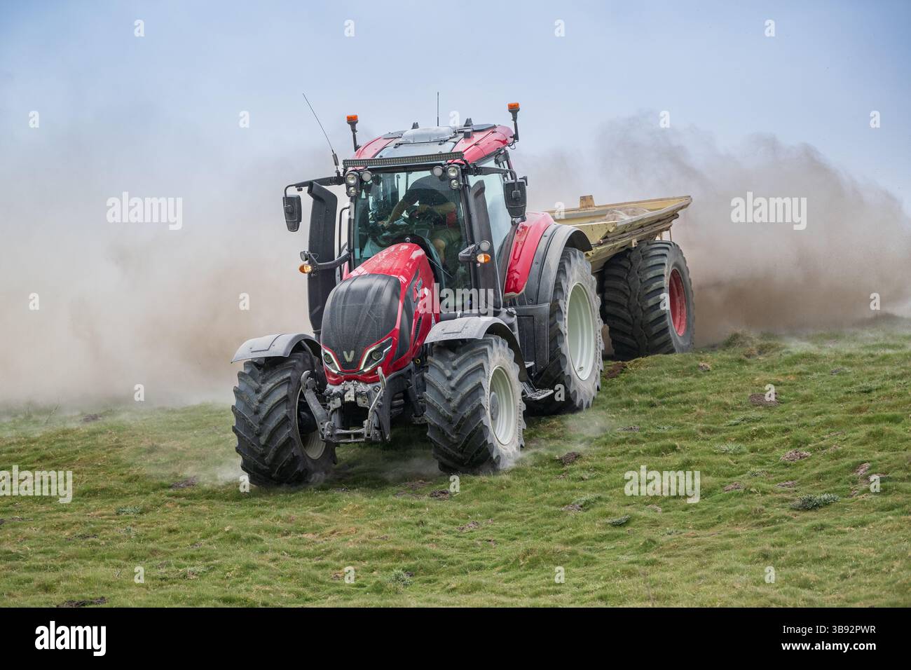 Appaltatore agricolo, alla guida di un trattore Valtra rosso, spalmando calce su un ripido pascolo per migliorare il pH del terreno e la qualità del terreno. Wensley Foto Stock