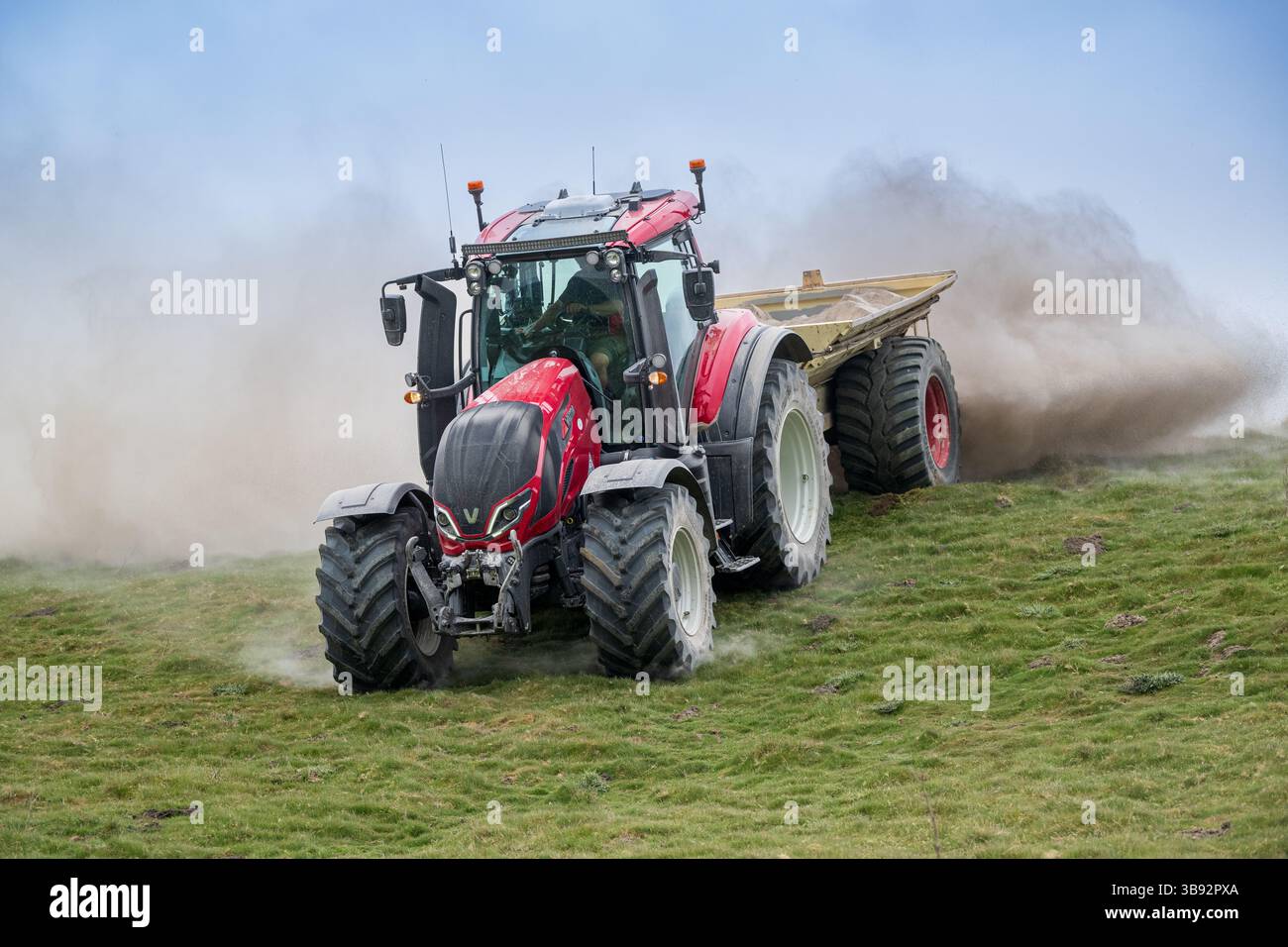 Appaltatore agricolo, alla guida di un trattore Valtra rosso, spalmando calce su un ripido pascolo per migliorare il pH del terreno e la qualità del terreno. Wensley Foto Stock