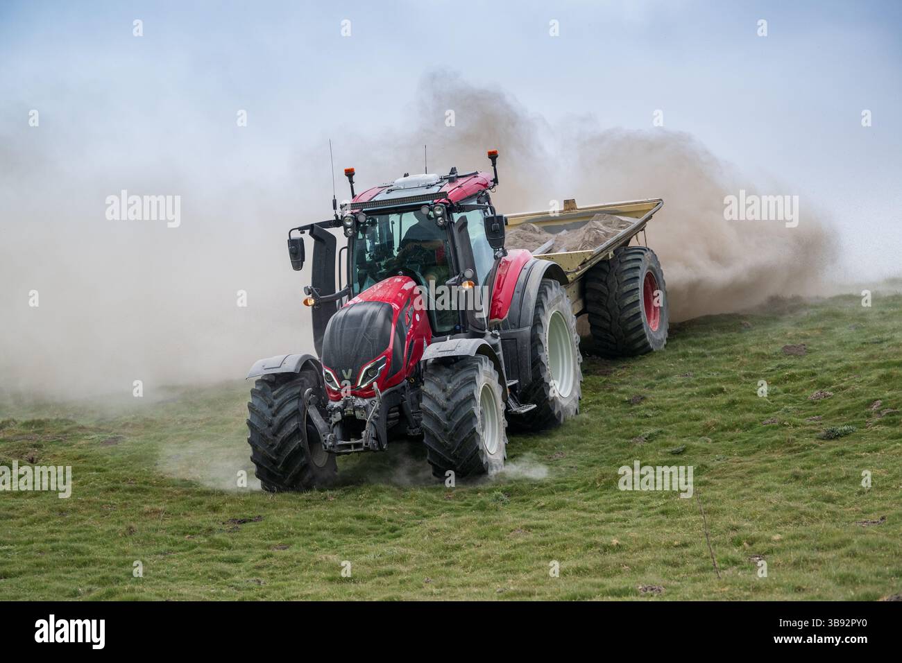 Appaltatore agricolo, alla guida di un trattore Valtra rosso, spalmando calce su un ripido pascolo per migliorare il pH del terreno e la qualità del terreno. Wensley Foto Stock
