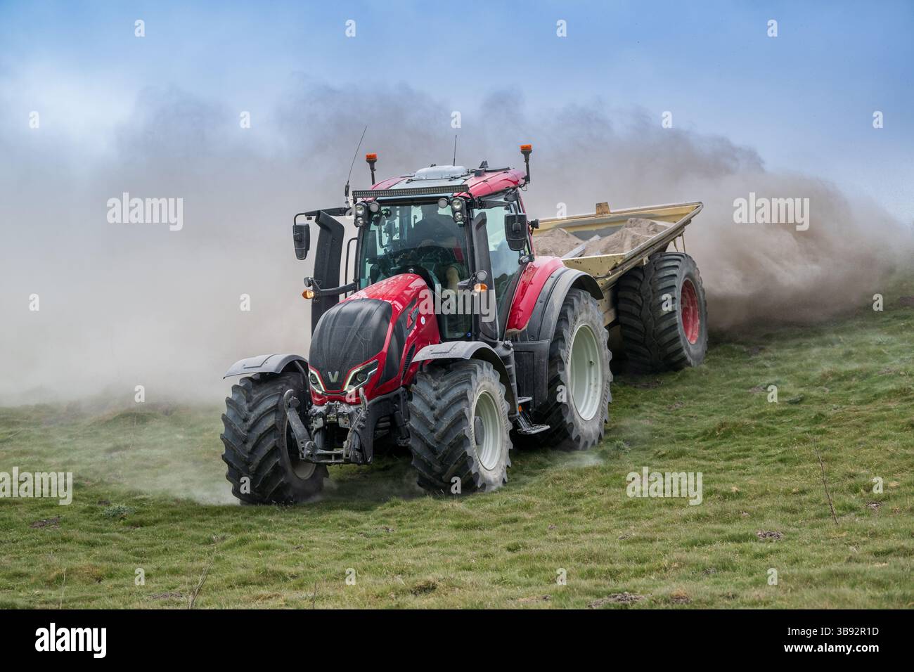 Appaltatore agricolo, alla guida di un trattore Valtra rosso, spalmando calce su un ripido pascolo per migliorare il pH del terreno e la qualità del terreno. Wensley Foto Stock