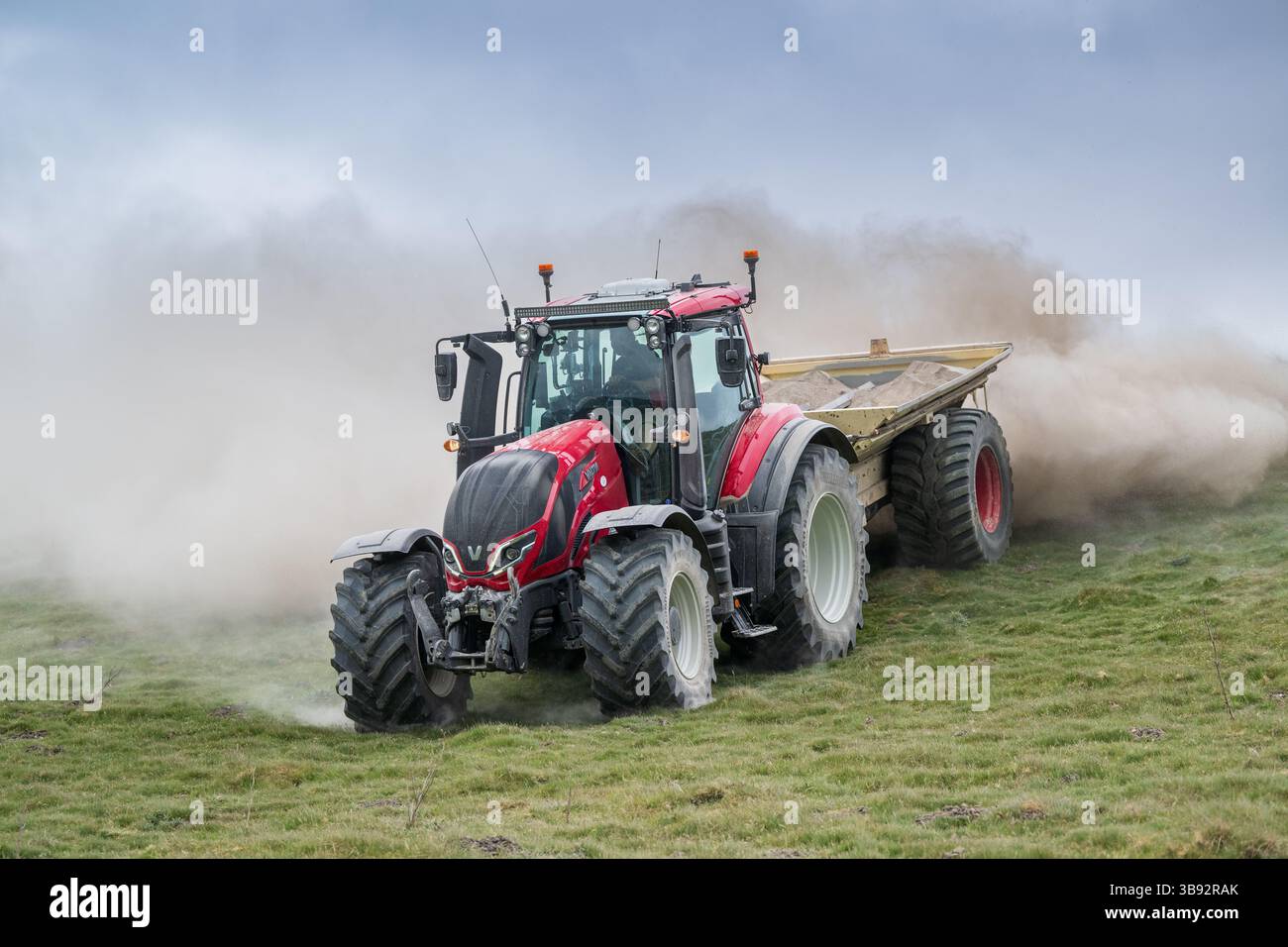 Appaltatore agricolo, alla guida di un trattore Valtra rosso, spalmando calce su un ripido pascolo per migliorare il pH del terreno e la qualità del terreno. Wensley Foto Stock