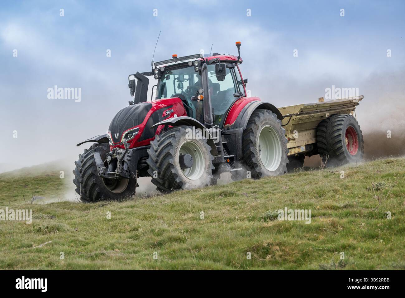 Appaltatore agricolo, alla guida di un trattore Valtra rosso, spalmando calce su un ripido pascolo per migliorare il pH del terreno e la qualità del terreno. Wensley Foto Stock