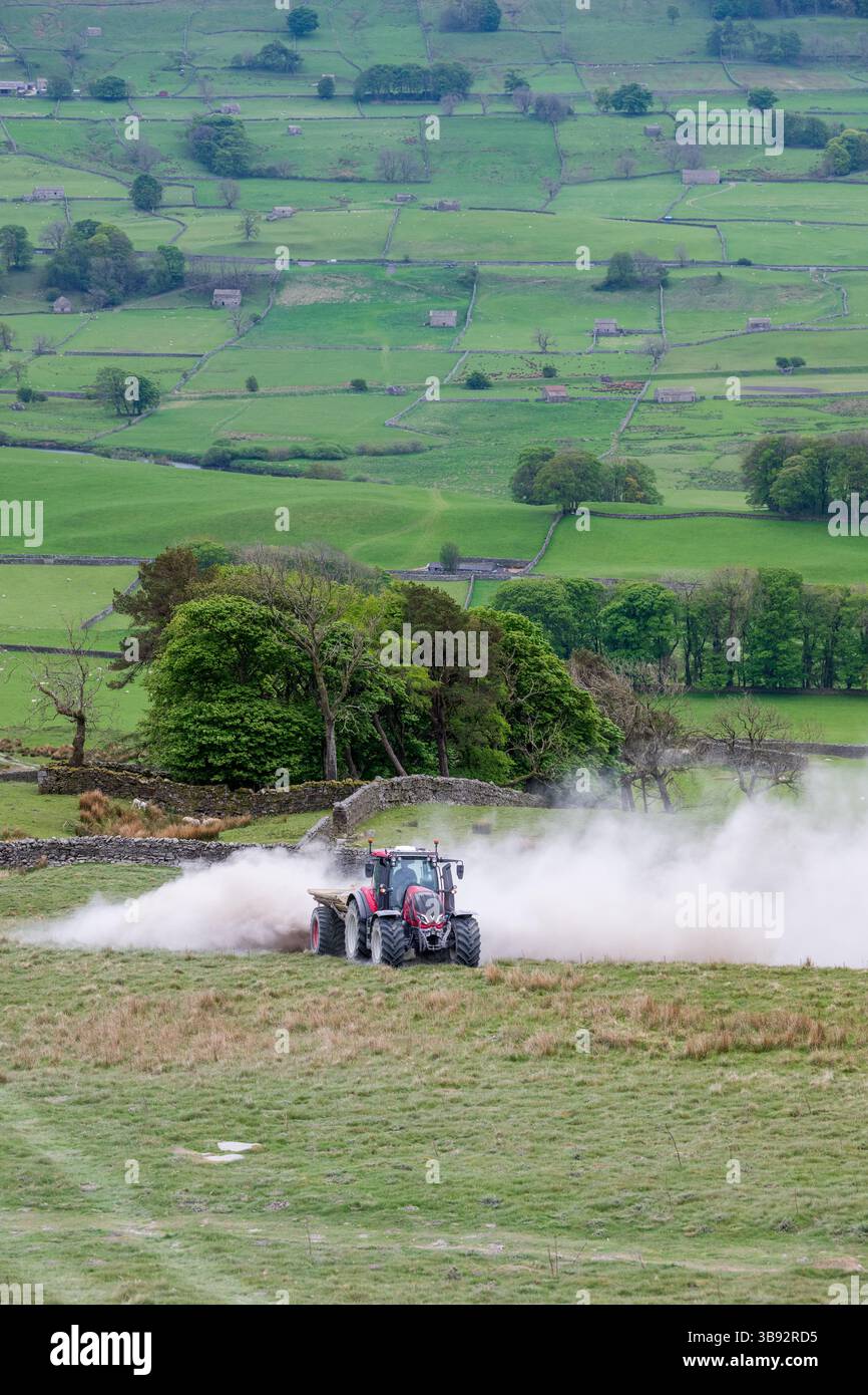 Appaltatore agricolo, alla guida di un trattore Valtra rosso, spalmando calce su un ripido pascolo per migliorare il pH del terreno e la qualità del terreno. Wensley Foto Stock