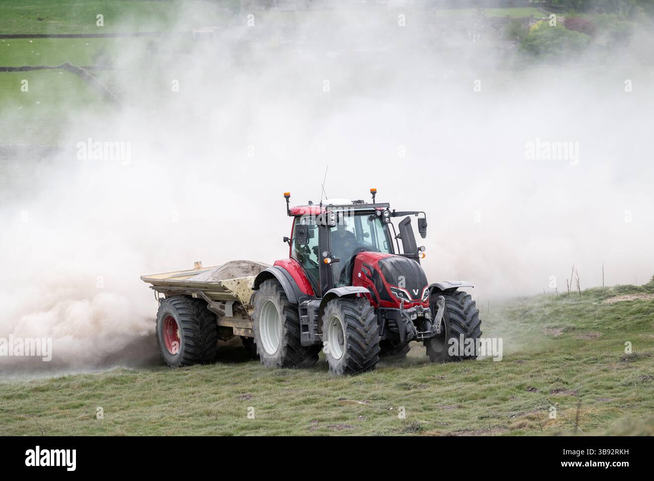 Appaltatore agricolo, alla guida di un trattore Valtra rosso, spalmando calce su un ripido pascolo per migliorare il pH del terreno e la qualità del terreno. Wensley Foto Stock