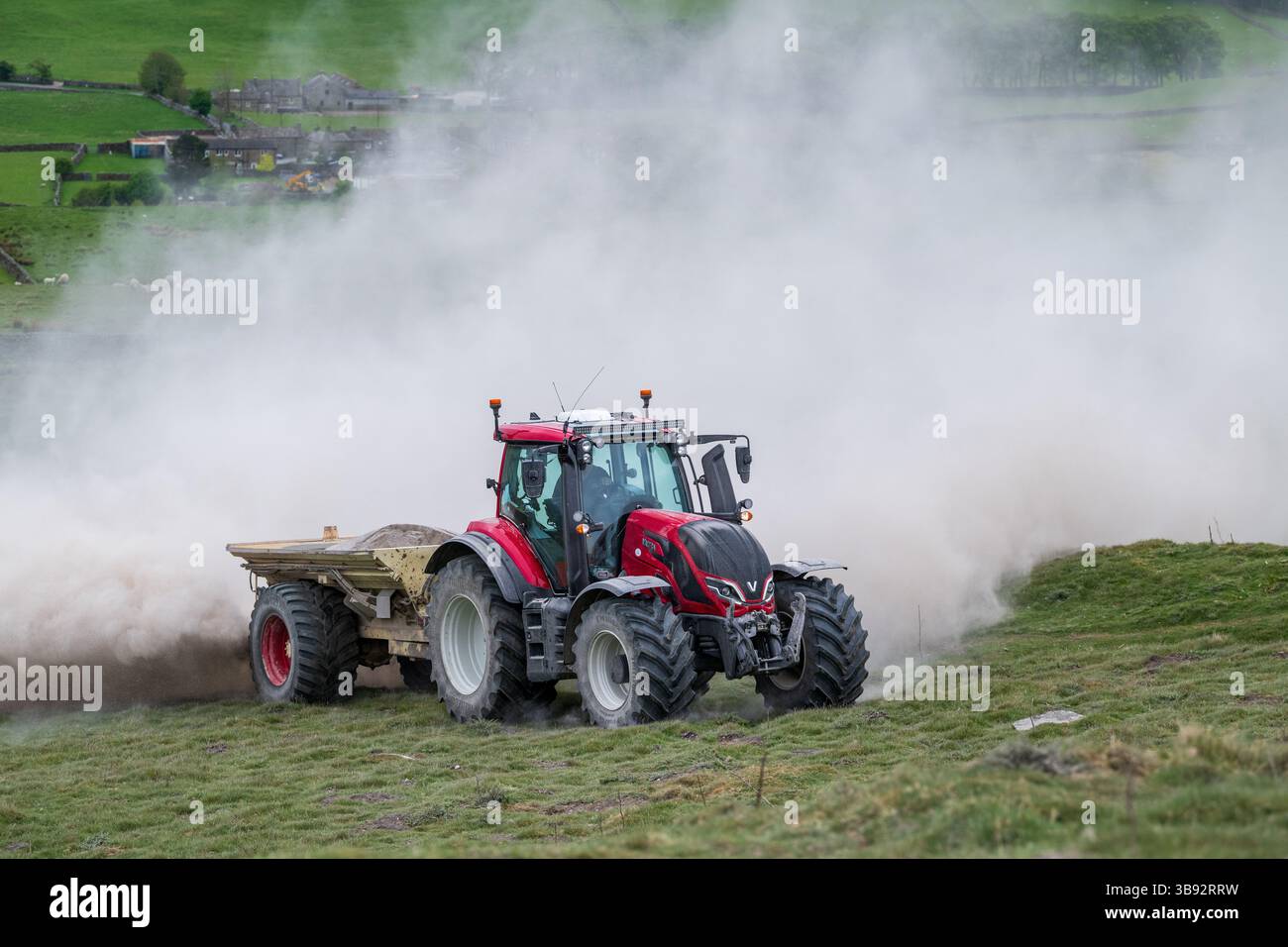 Appaltatore agricolo, alla guida di un trattore Valtra rosso, spalmando calce su un ripido pascolo per migliorare il pH del terreno e la qualità del terreno. Wensley Foto Stock