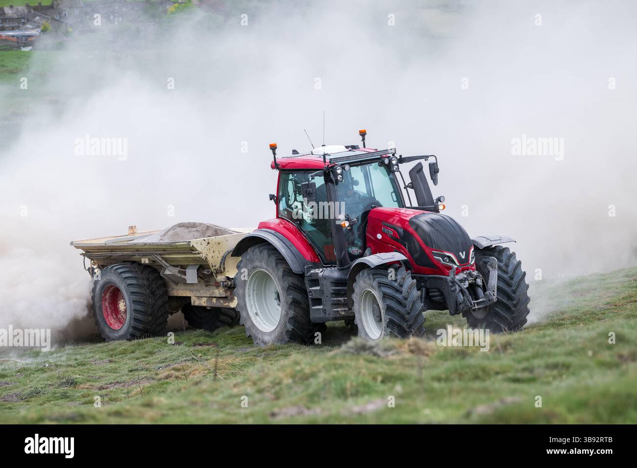 Appaltatore agricolo, alla guida di un trattore Valtra rosso, spalmando calce su un ripido pascolo per migliorare il pH del terreno e la qualità del terreno. Wensley Foto Stock