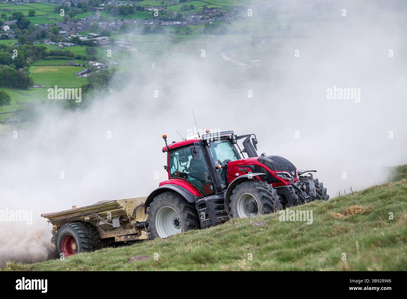 Appaltatore agricolo, alla guida di un trattore Valtra rosso, spalmando calce su un ripido pascolo per migliorare il pH del terreno e la qualità del terreno. Wensley Foto Stock