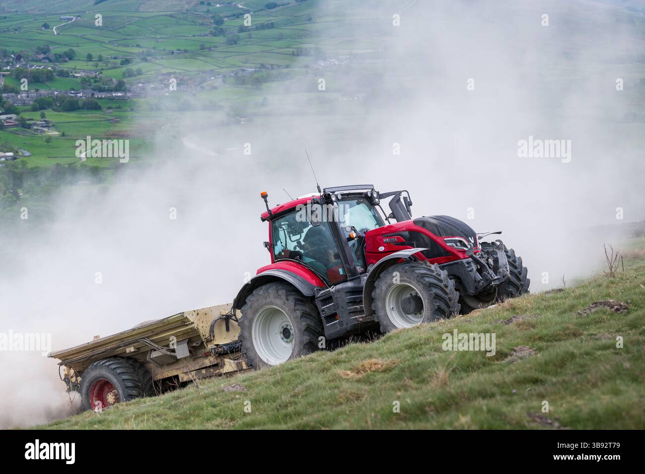 Appaltatore agricolo, alla guida di un trattore Valtra rosso, spalmando calce su un ripido pascolo per migliorare il pH del terreno e la qualità del terreno. Wensley Foto Stock