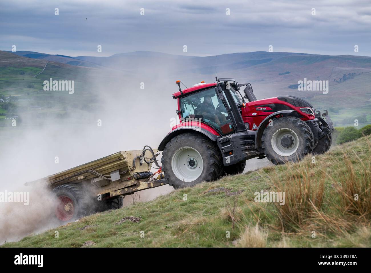 Appaltatore agricolo, alla guida di un trattore Valtra rosso, spalmando calce su un ripido pascolo per migliorare il pH del terreno e la qualità del terreno. Wensley Foto Stock