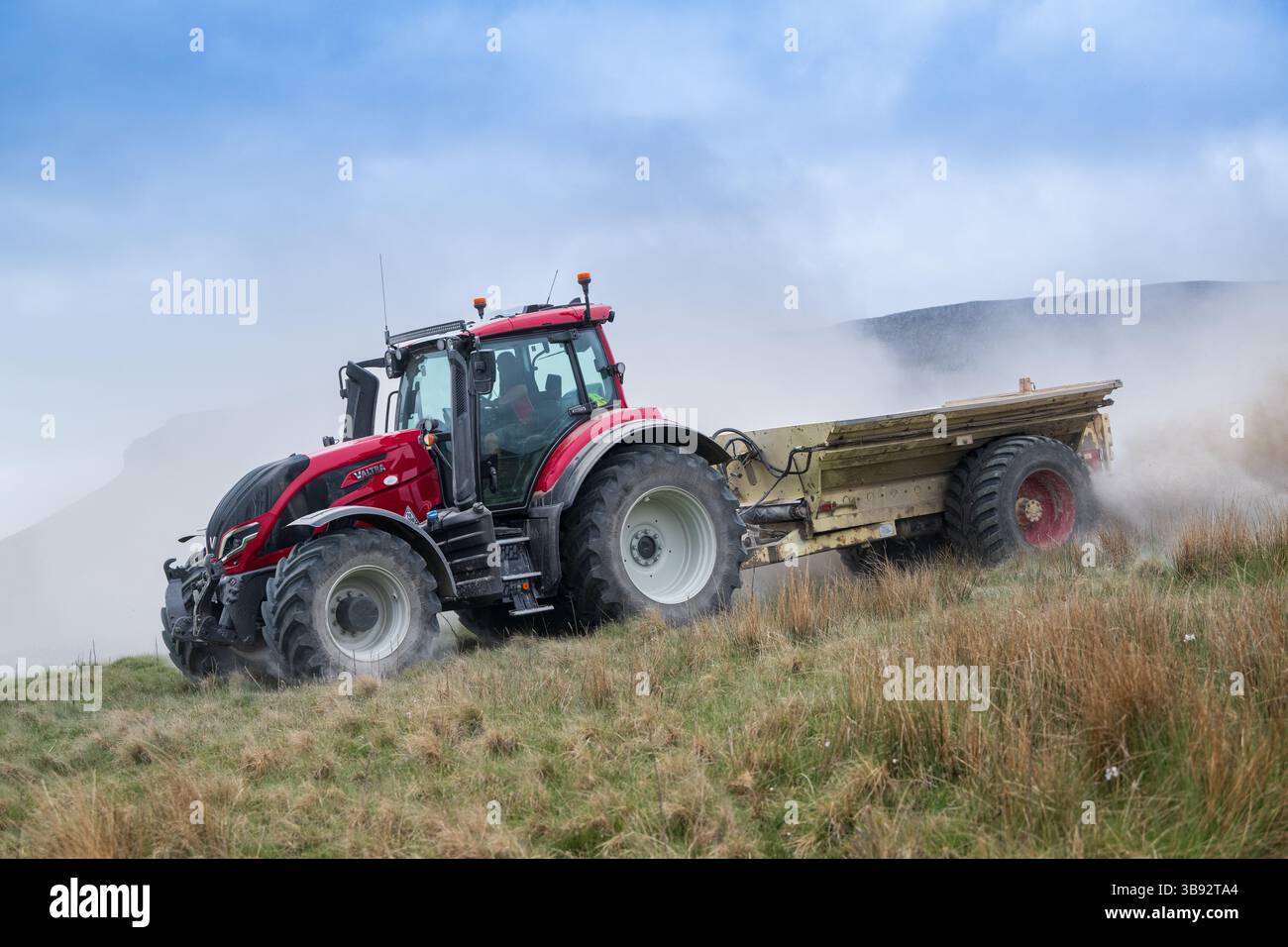Appaltatore agricolo, alla guida di un trattore Valtra rosso, spalmando calce su un ripido pascolo per migliorare il pH del terreno e la qualità del terreno. Wensley Foto Stock