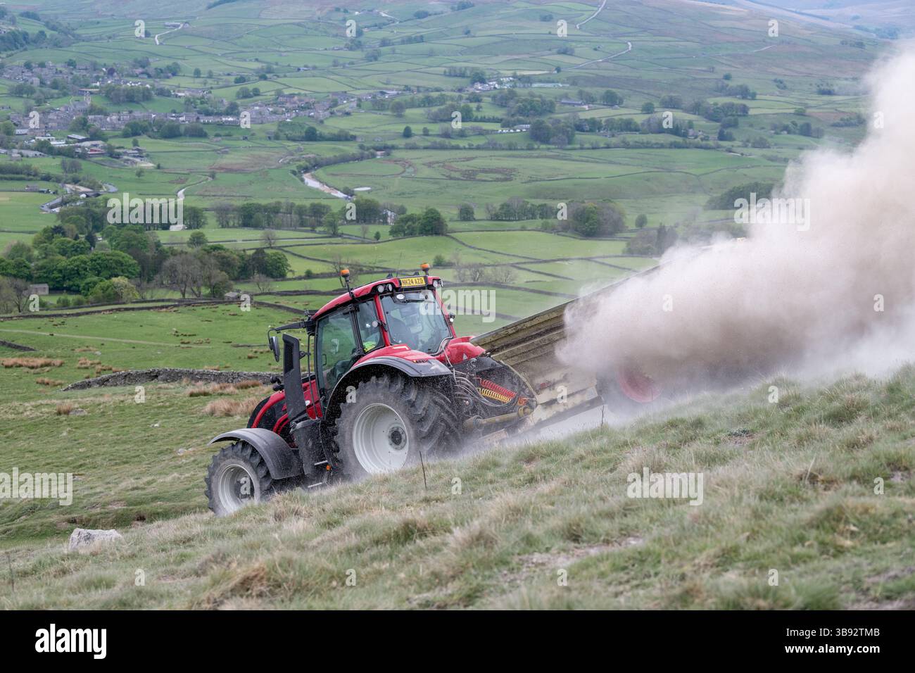 Appaltatore agricolo, alla guida di un trattore Valtra rosso, spalmando calce su un ripido pascolo per migliorare il pH del terreno e la qualità del terreno. Wensley Foto Stock