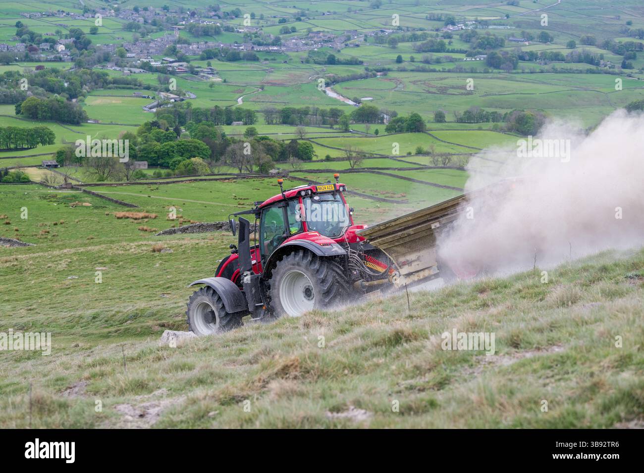 Appaltatore agricolo, alla guida di un trattore Valtra rosso, spalmando calce su un ripido pascolo per migliorare il pH del terreno e la qualità del terreno. Wensley Foto Stock