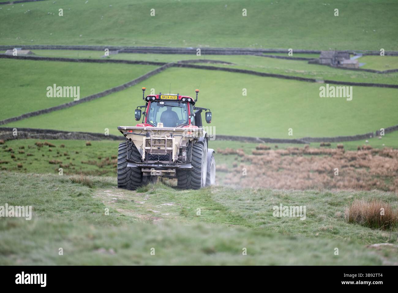 Appaltatore agricolo, alla guida di un trattore Valtra rosso, spalmando calce su un ripido pascolo per migliorare il pH del terreno e la qualità del terreno. Wensley Foto Stock