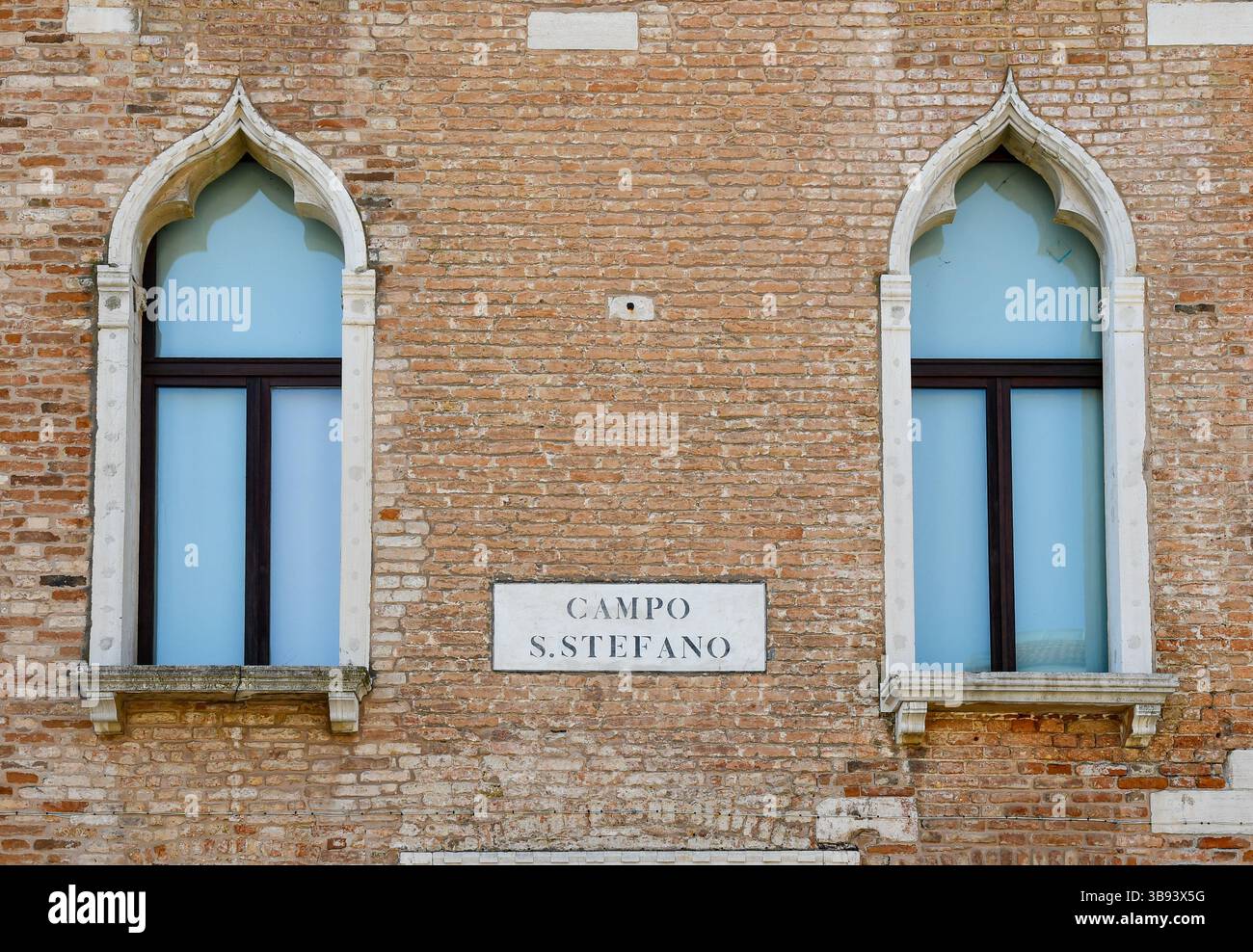 Un paio di finestre gotiche veneziane sulla facciata di un palazzo in mattoni, con il segno di campo Santo Stefano, San Marco sestiere, Venezia, Veneto, Italia Foto Stock