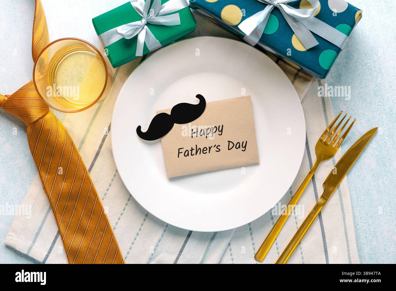Buona festa del papà. Vista dall'alto del piatto bianco con busta e baffi con la bella festa del papà accanto a cravatta, scatole da regalo e posate Foto Stock