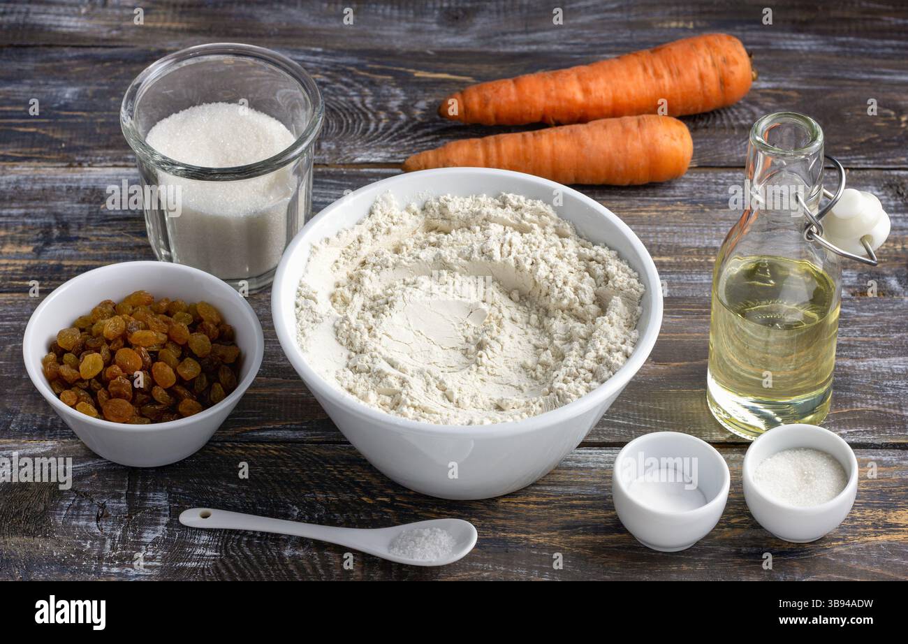 Set di ingredienti per la torta di carote su tavola rustica in legno: Farina, zucchero, carote, uvetta, olio. Cottura in casa, concetto di cottura, ingredienti naturali Foto Stock