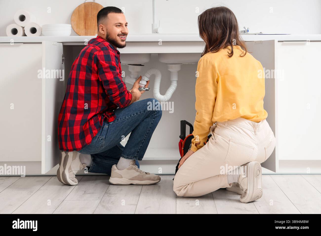Giovane donna e idraulico che ripara il tubo del lavandino in cucina Foto Stock