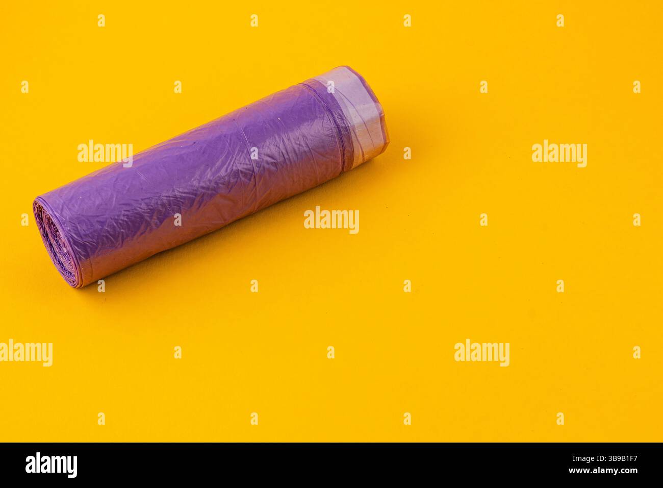 Un foglio di plastica viola ben arrotolato si appoggia su uno sfondo giallo brillante, che mostra la sua texture lucida e il vibrante contrasto di colore, ideale per l'artigianato Foto Stock