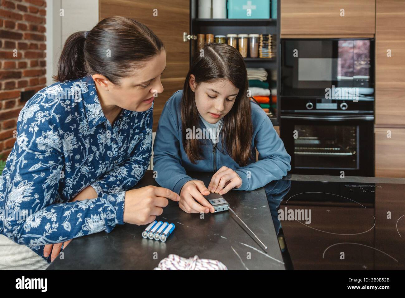 Madre e figlia ascoltano notizie di emergenza in un piccolo ricevitore radio portatile durante il blackout elettrico. Famiglia pronta con dispensa alimentare di emergenza in k Foto Stock