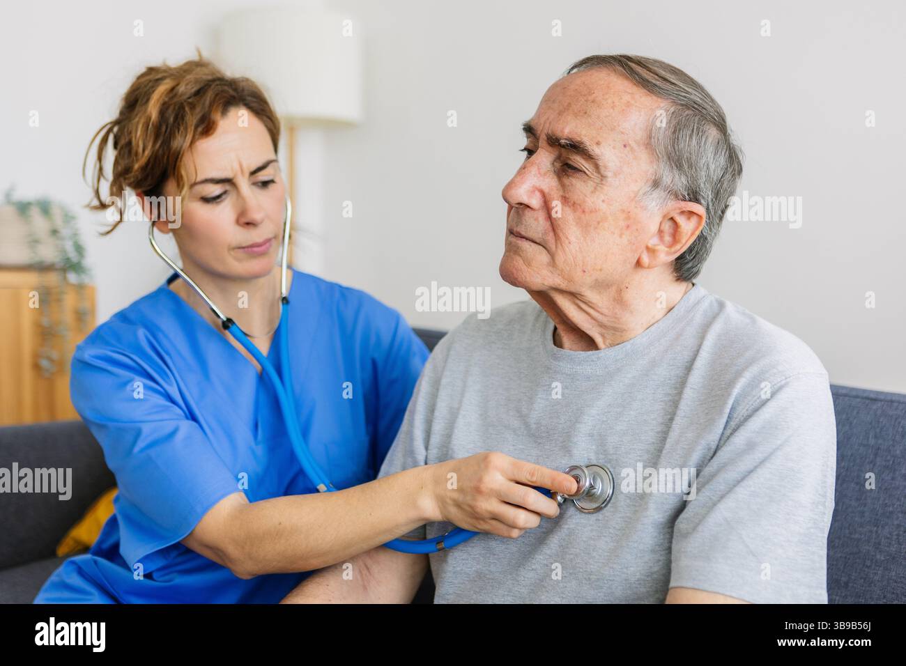 Giovane donna medico che ascolta il suono del cuore al paziente anziano a casa Foto Stock