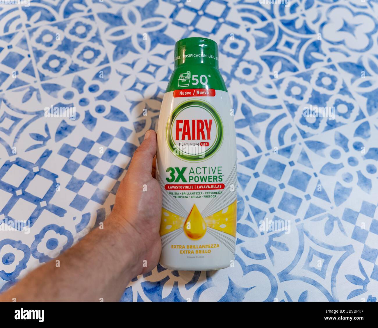 Mano che regge una bottiglia di detergente per lavastoviglie Fairy Platinum Gel su sfondo blu Foto Stock