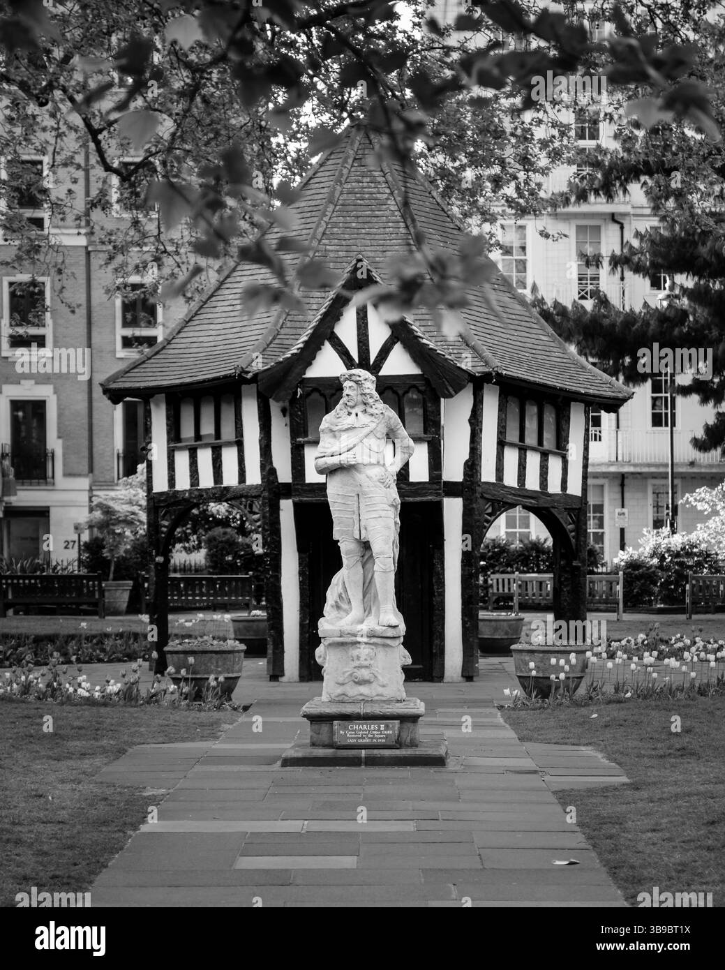 Londra, Inghilterra - 28 aprile 2025: Una statua di Carlo II dello scultore danese Caius Gabriel Cibber si erge di fronte alla capanna del giardiniere in stile Tudor Foto Stock