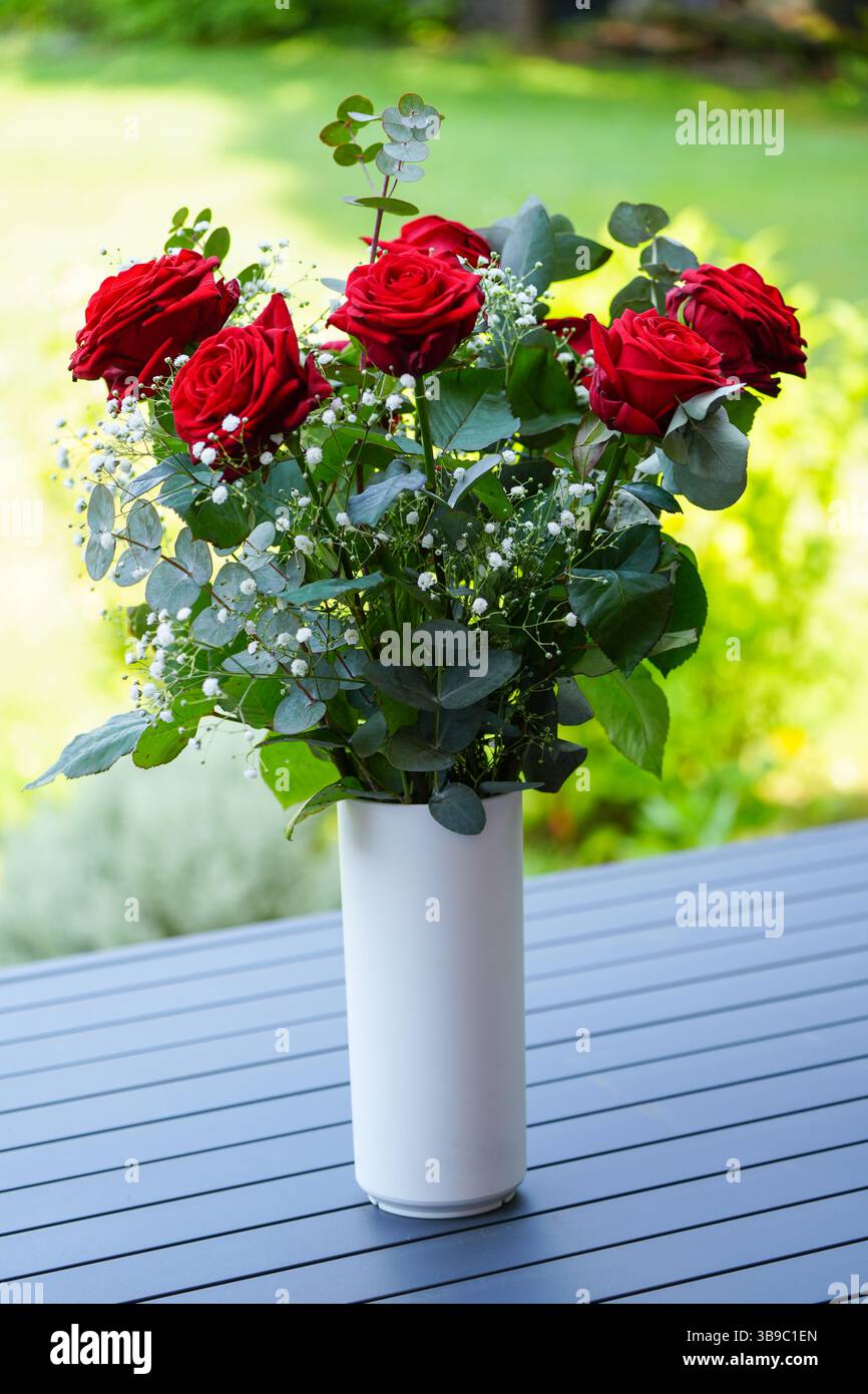 Un bouquet di rose rosse in un vaso bianco sul tavolo da giardino Foto Stock