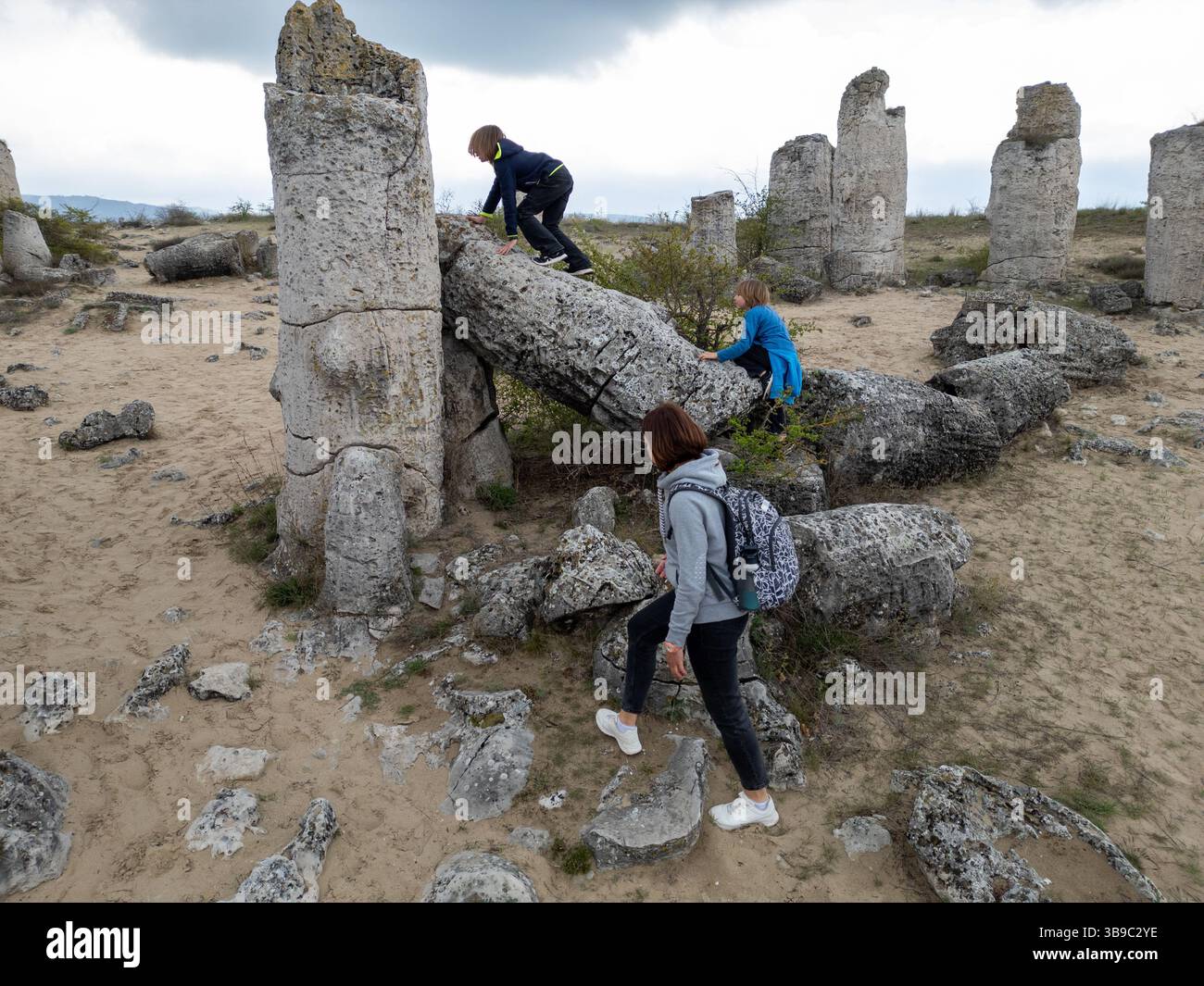 Madre e due bambini esplorano il terreno roccioso in un paesaggio arido e semi-desertico. I bambini giocano su formazioni di pietra mentre la madre guarda, enjo Foto Stock