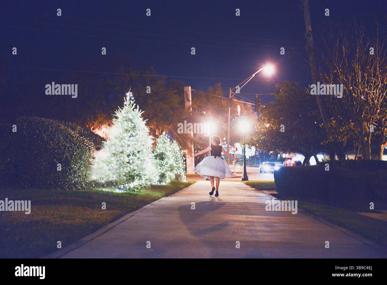 Ragazza in abito bianco che corre lungo un marciapiede illuminato di notte. Foto Stock