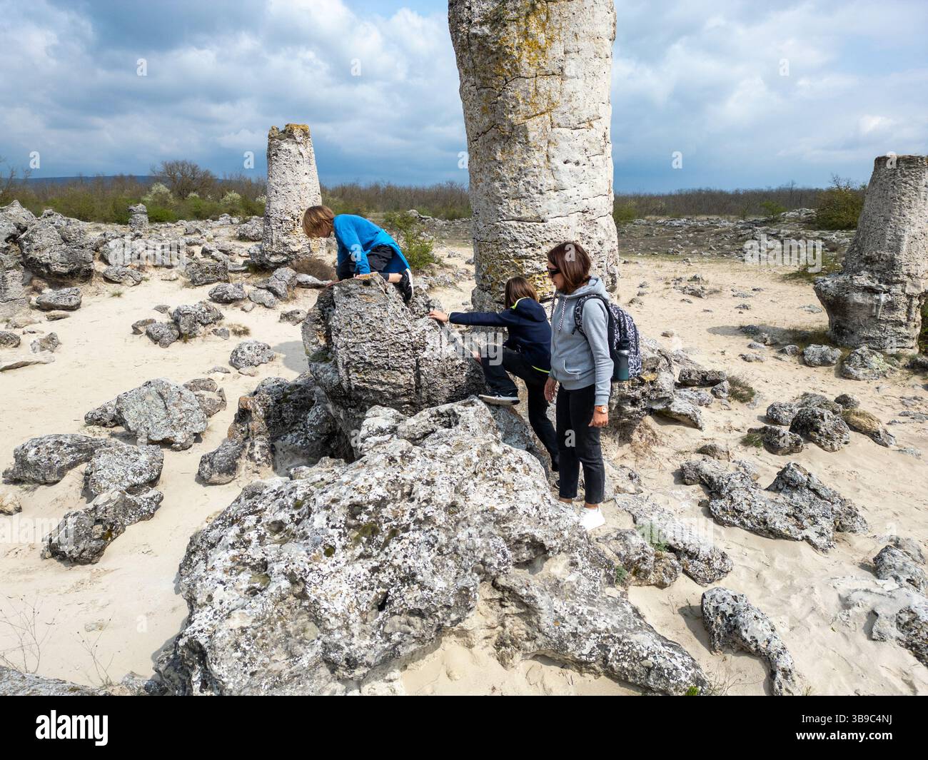 Madre e due bambini esplorano il terreno roccioso in un paesaggio arido e semi-desertico. I bambini giocano su formazioni di pietra mentre la madre guarda, enjo Foto Stock