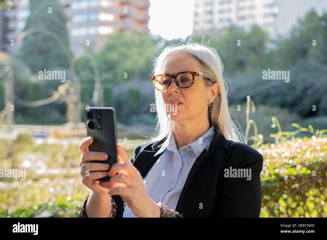 Donna d'affari concentrata che usa lo smartphone nel parco cittadino Foto Stock